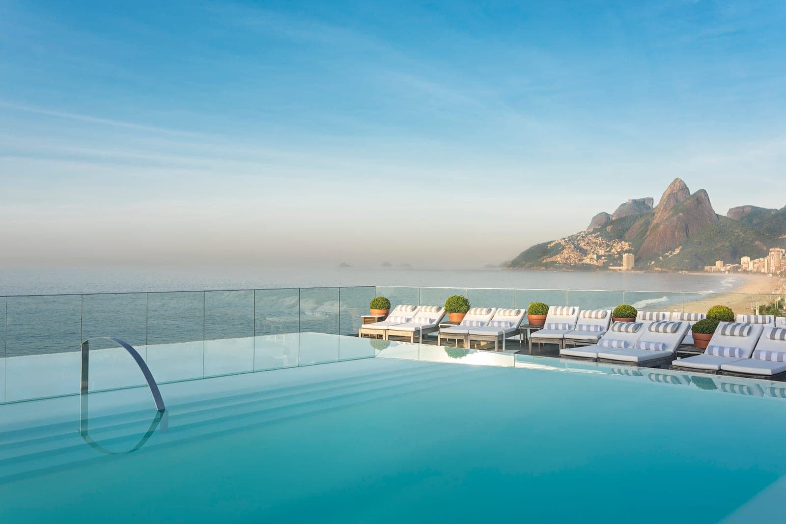 An infinity pool overlooking the ocean with loungers and mountains behind