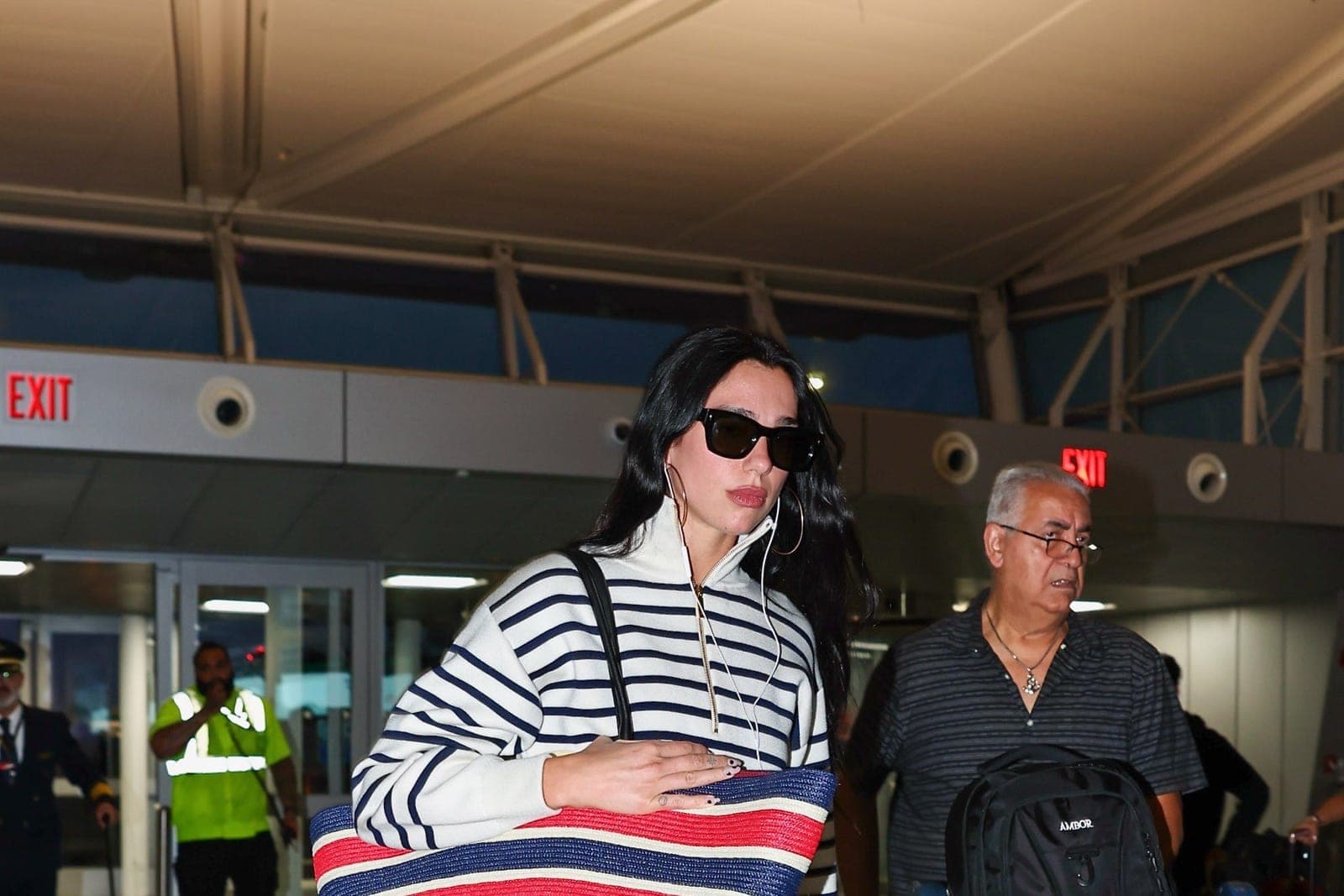 Dua Lipa photographed at JFK Airport carrying an oversized striped raffia Chanel tote