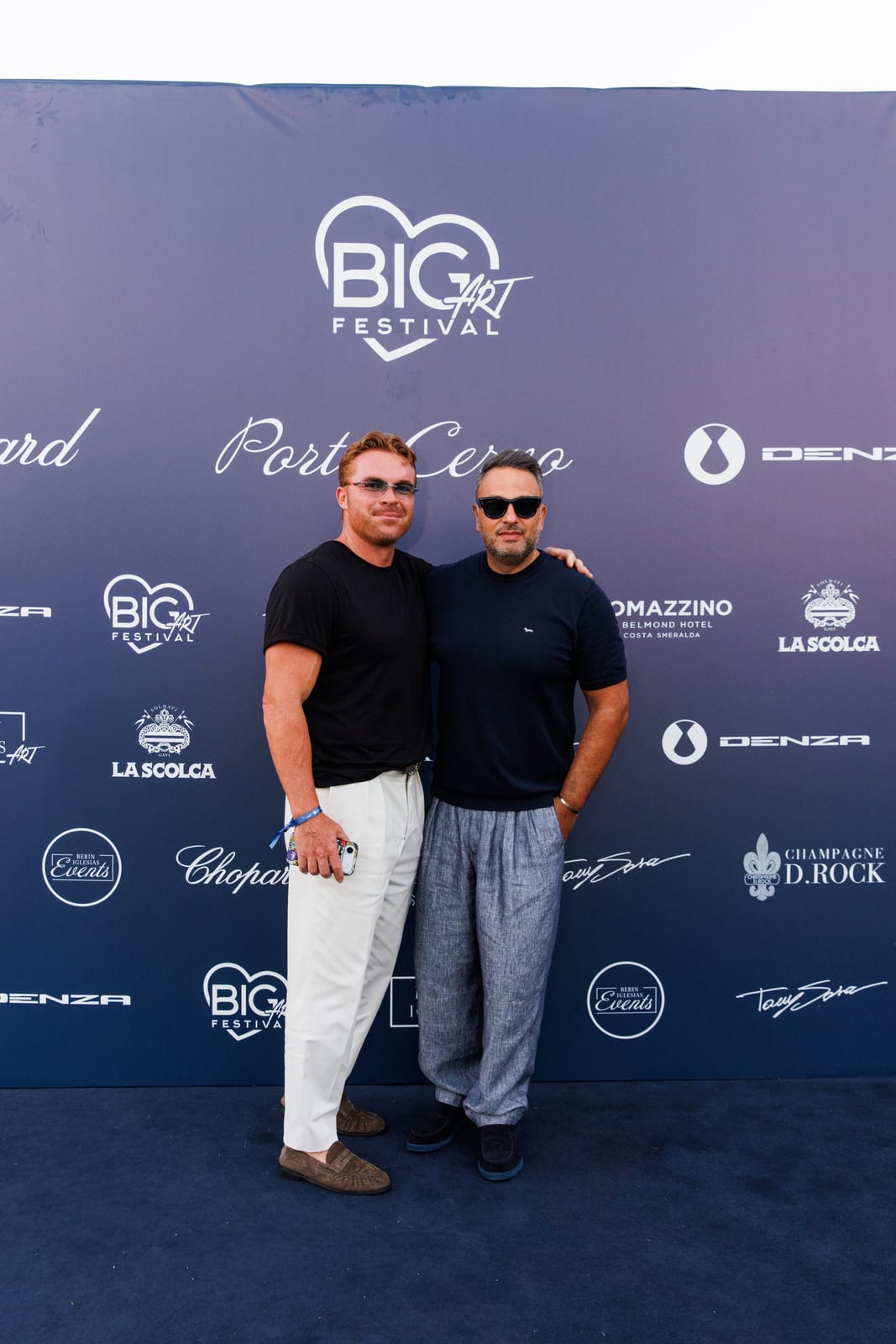 Two guests photographed together on the BIG ART Festival press wall in Porto Cervo