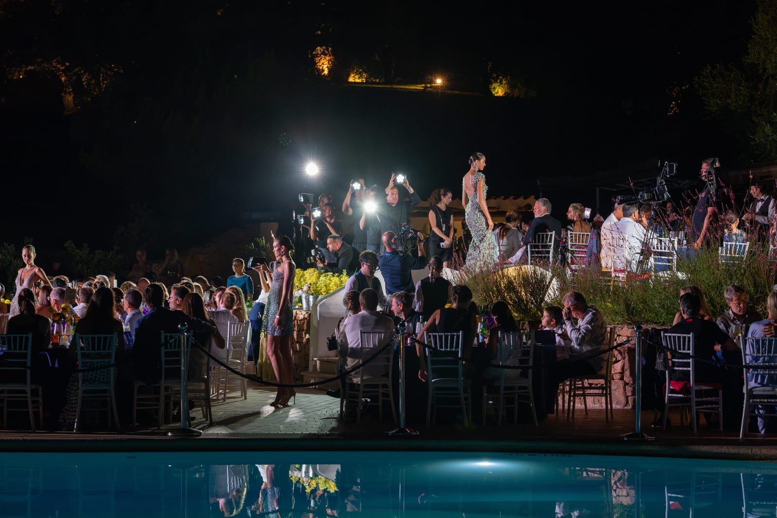 Models walking a poolside runway past seated guests and photographers
